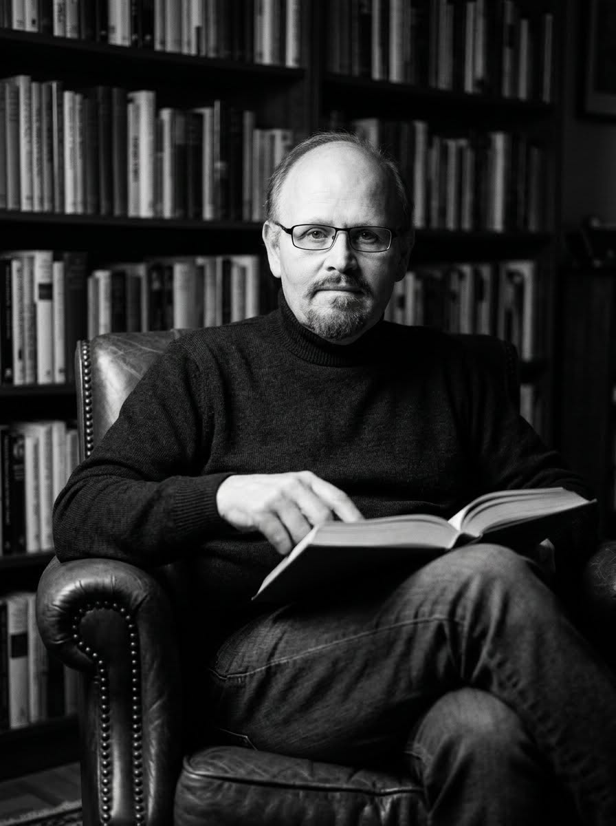 Portrait of C.D. Lombardi, seated with an open book in a book-lined study.